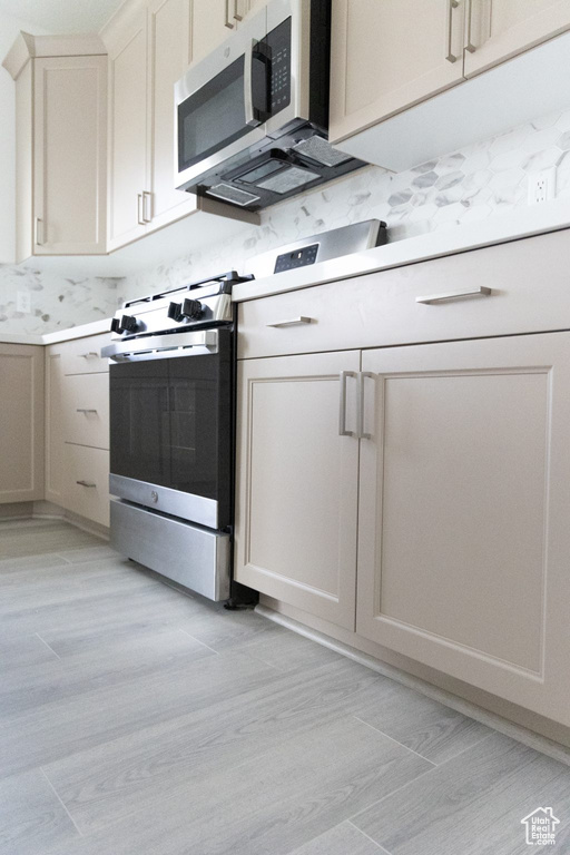Kitchen featuring backsplash, stainless steel appliances, light hardwood / wood-style floors, and light stone counters