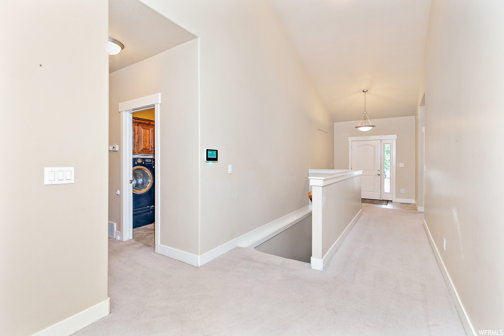 Hall with light colored carpet, vaulted ceiling, and washer / dryer