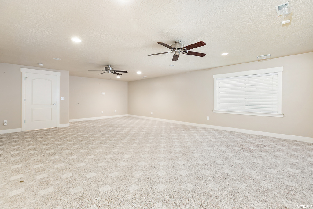 Empty room featuring light carpet, a textured ceiling, and ceiling fan