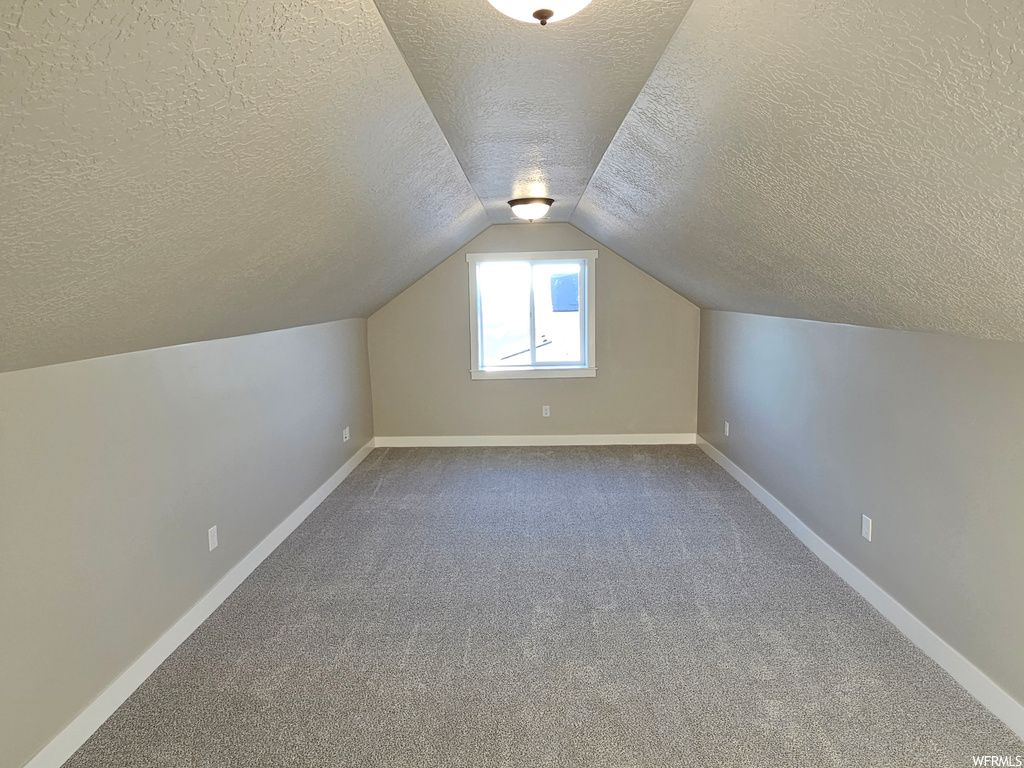 Bonus room featuring dark carpet, vaulted ceiling, and a textured ceiling