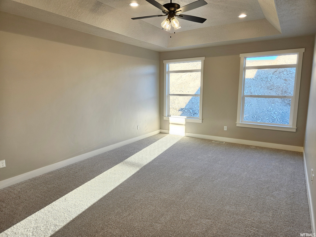 Carpeted empty room featuring ceiling fan, a textured ceiling, a raised ceiling, and plenty of natural light