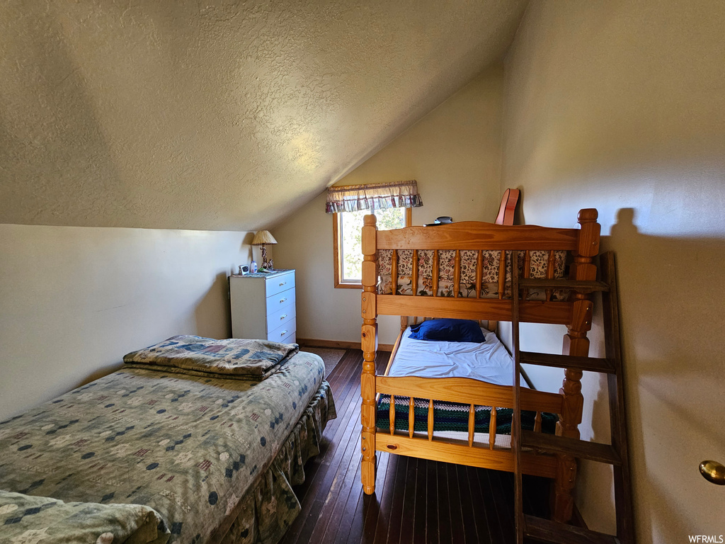 Bedroom featuring lofted ceiling, dark hardwood floors, and a textured ceiling