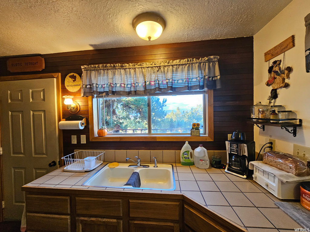 Kitchen featuring wood walls, tile countertops, and sink