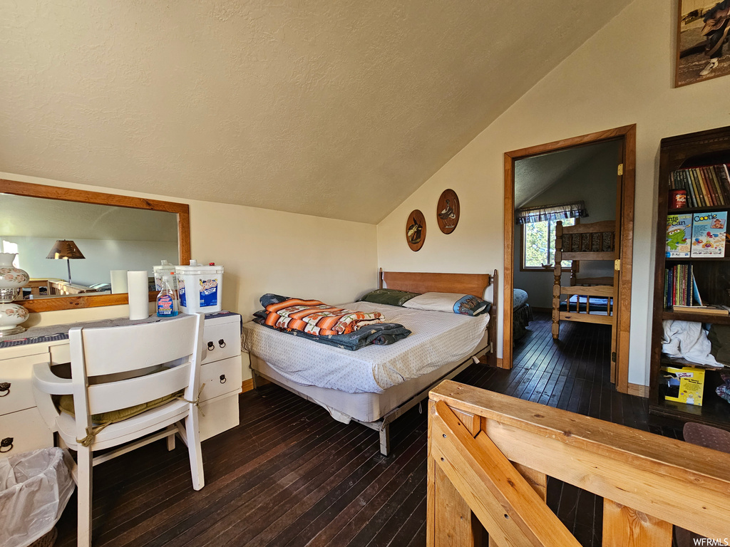 Bedroom featuring lofted ceiling, dark hardwood floors, and a textured ceiling