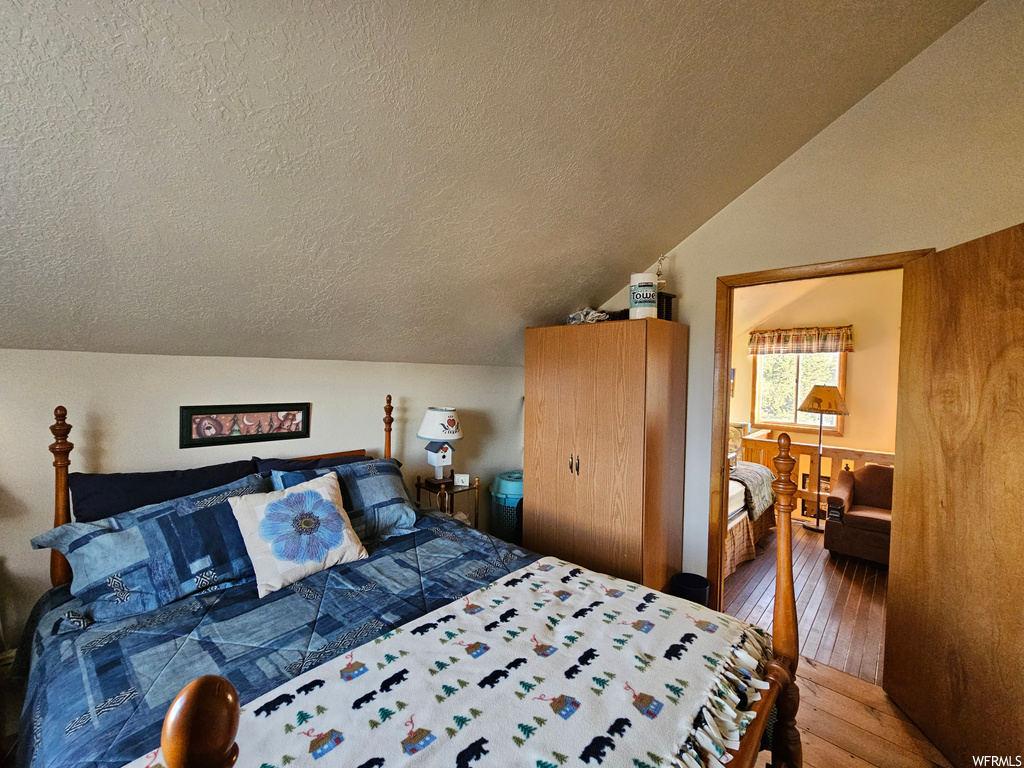 Hardwood floored bedroom featuring a textured ceiling and vaulted ceiling