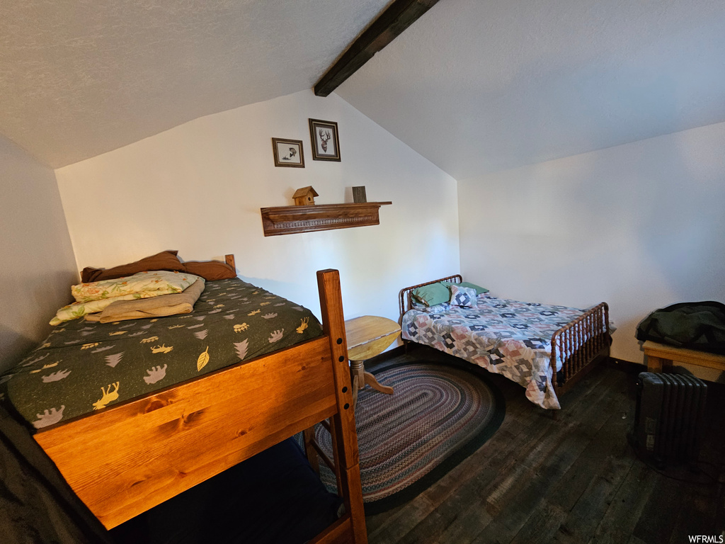 Hardwood floored bedroom featuring vaulted ceiling with beams and a textured ceiling