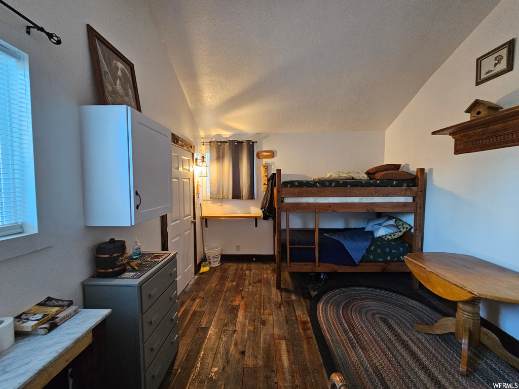 Bedroom with lofted ceiling, dark hardwood floors, and a textured ceiling