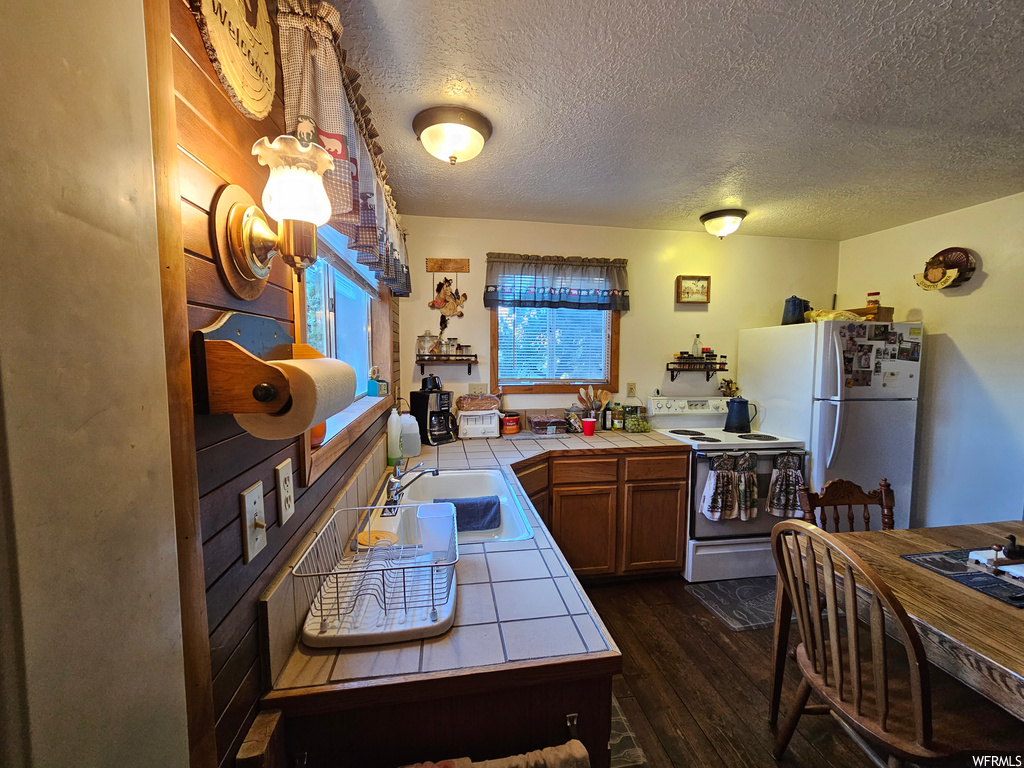 Kitchen with dark hardwood flooring, a textured ceiling, tile counters, white appliances, and sink