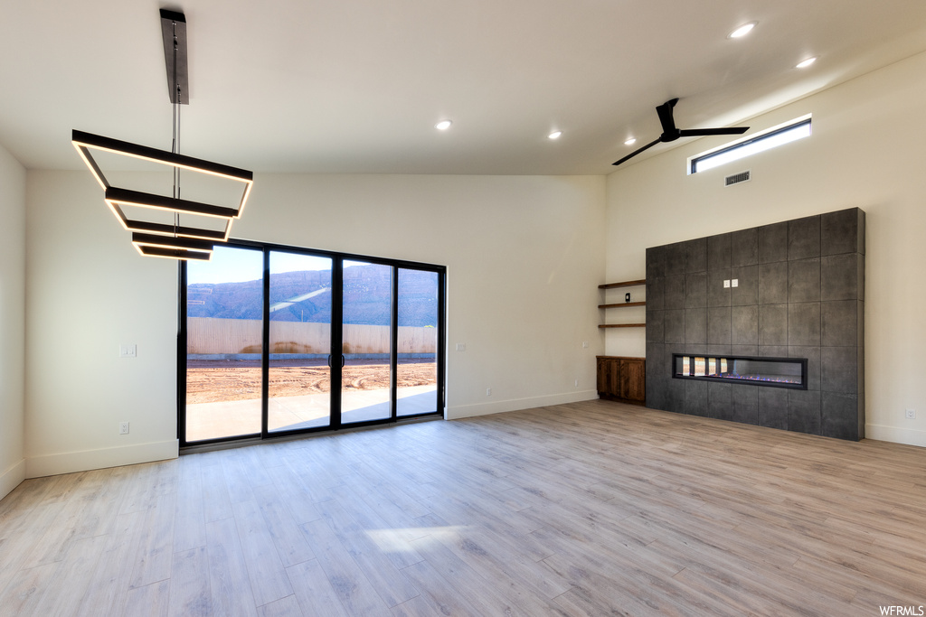 Unfurnished living room with a fireplace, vaulted ceiling high, ceiling fan, light hardwood flooring, and a mountain view