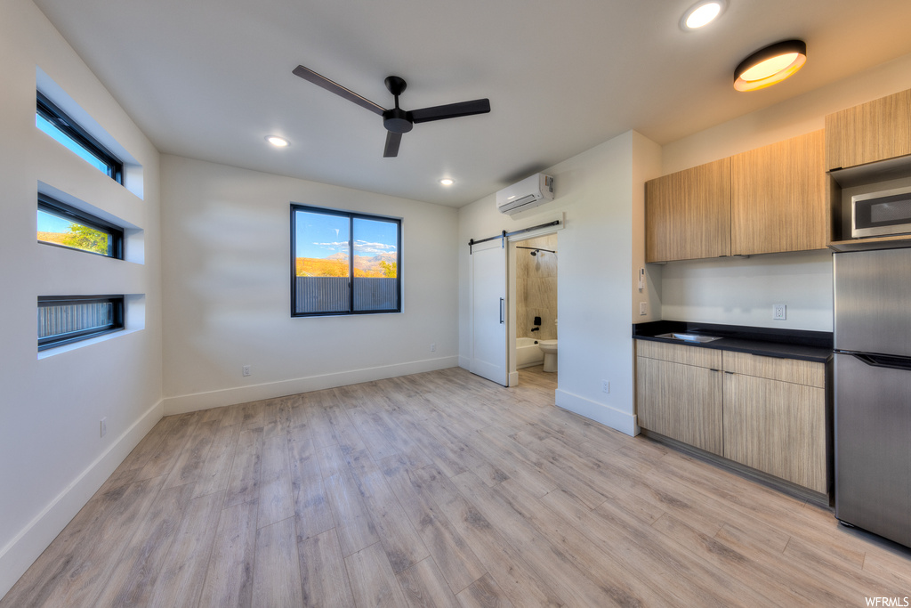 Kitchen featuring a barn door, light hardwood floors, ceiling fan, an AC wall unit, and appliances with stainless steel finishes