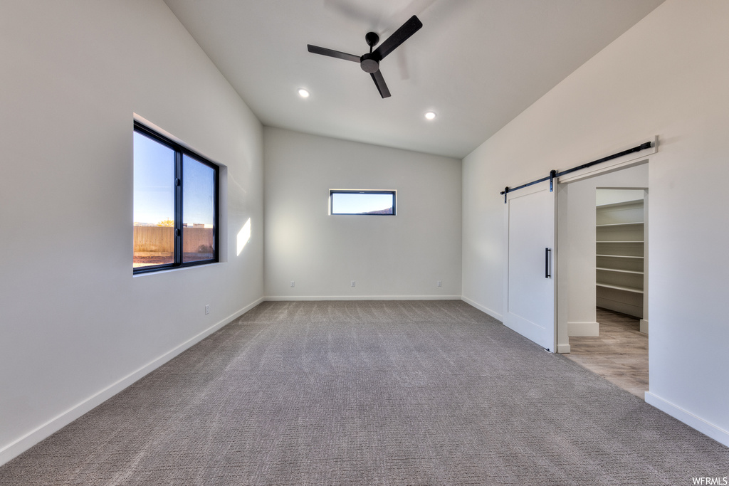 Carpeted empty room with a barn door, ceiling fan, and lofted ceiling