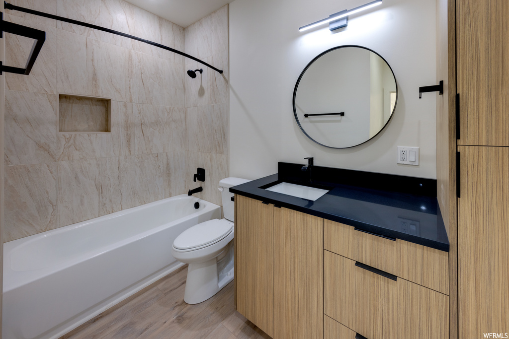 Full bathroom with wood-type flooring, tiled shower / bath, vanity, and toilet