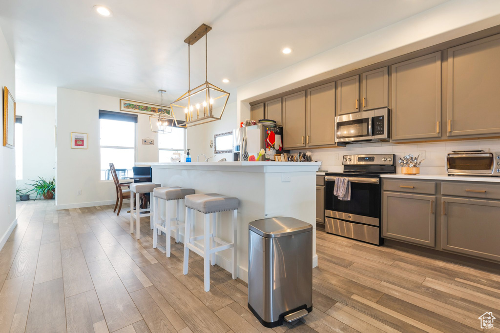 Kitchen featuring a kitchen breakfast bar, stainless steel appliances, decorative light fixtures, an inviting chandelier, and light hardwood / wood-style flooring