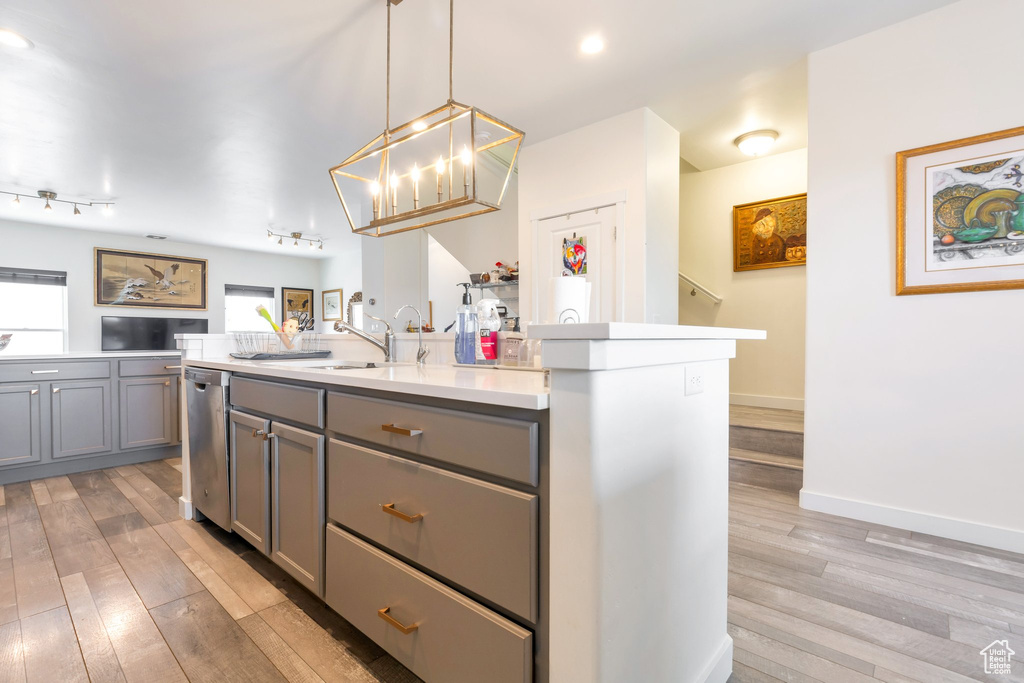 Kitchen featuring a kitchen island with sink, gray cabinets, pendant lighting, stainless steel dishwasher, and light hardwood / wood-style flooring