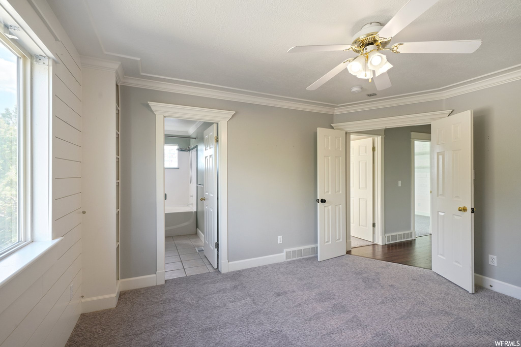 Unfurnished bedroom featuring ornamental molding, ensuite bathroom, ceiling fan, and carpet flooring