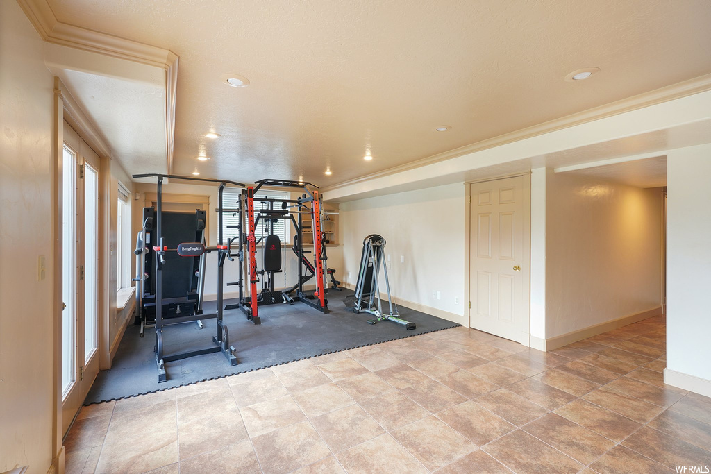 Workout area featuring crown molding and light tile floors