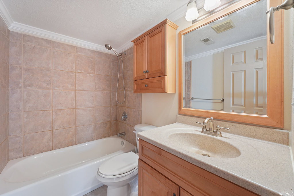 Full bathroom with a textured ceiling, toilet, vanity, and tiled shower / bath combo