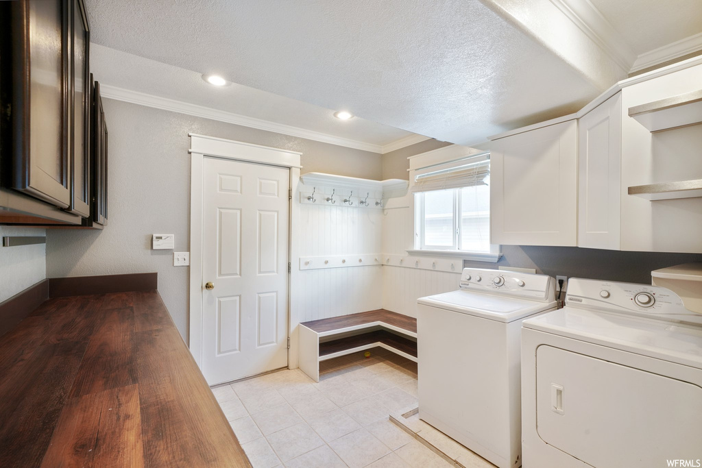 Laundry area with washing machine and dryer, a textured ceiling, ornamental molding, and light tile floors