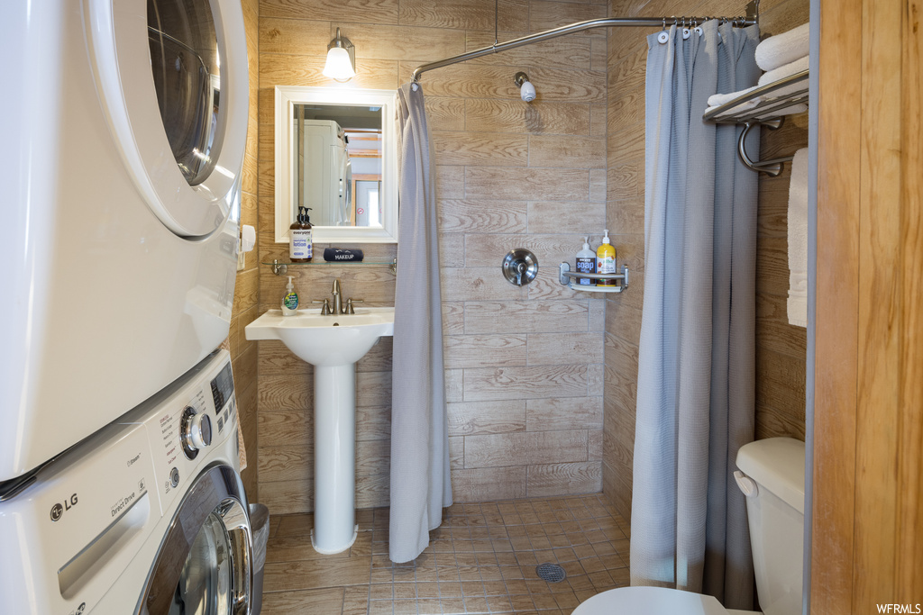 Bathroom featuring toilet, a shower with shower curtain, sink, and stacked washer and dryer