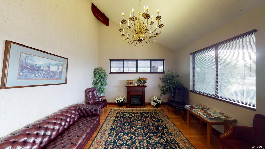 Sitting room with hardwood flooring, a notable chandelier, vaulted ceiling, and a fireplace