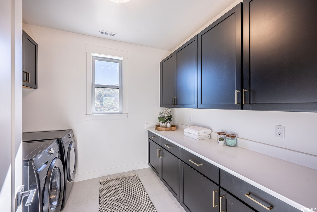Laundry area with washing machine and dryer, cabinets, and light tile floors
