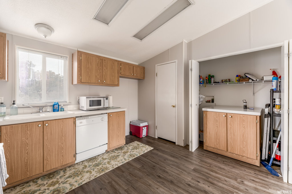 Kitchen featuring white appliances, sink, vaulted ceiling, and dark hardwood floors