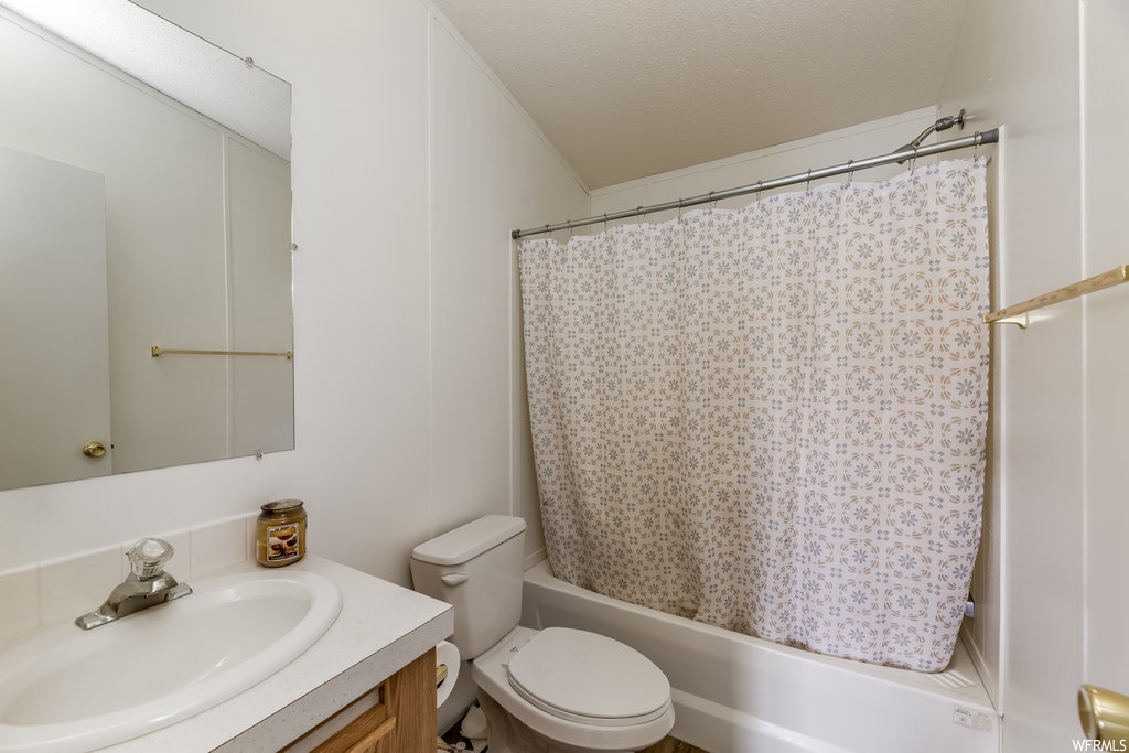 Full bathroom with shower / tub combo with curtain, a textured ceiling, vanity, and toilet