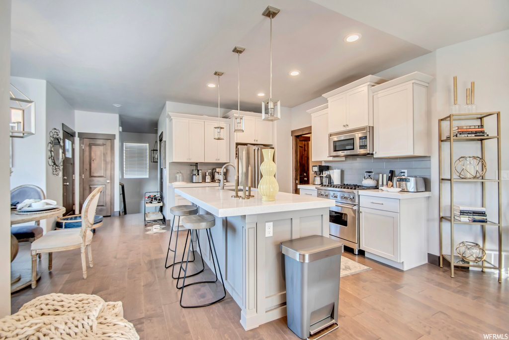 Kitchen with white cabinetry, premium appliances, a kitchen island with sink, and light hardwood flooring