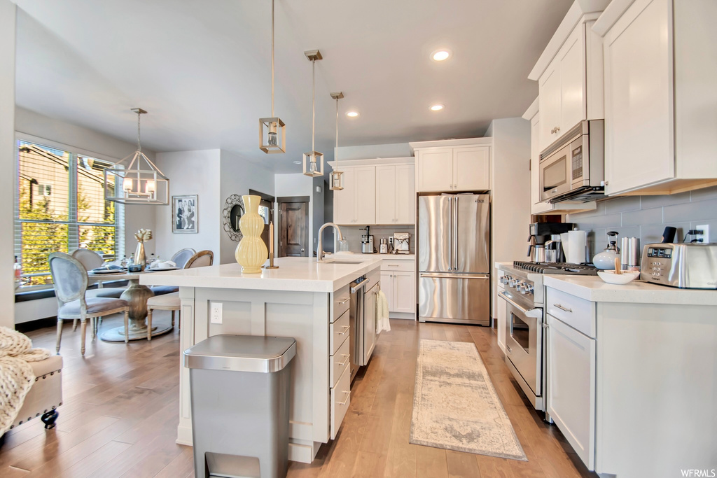 Kitchen featuring decorative light fixtures, a center island with sink, backsplash, a notable chandelier, and stainless steel appliances