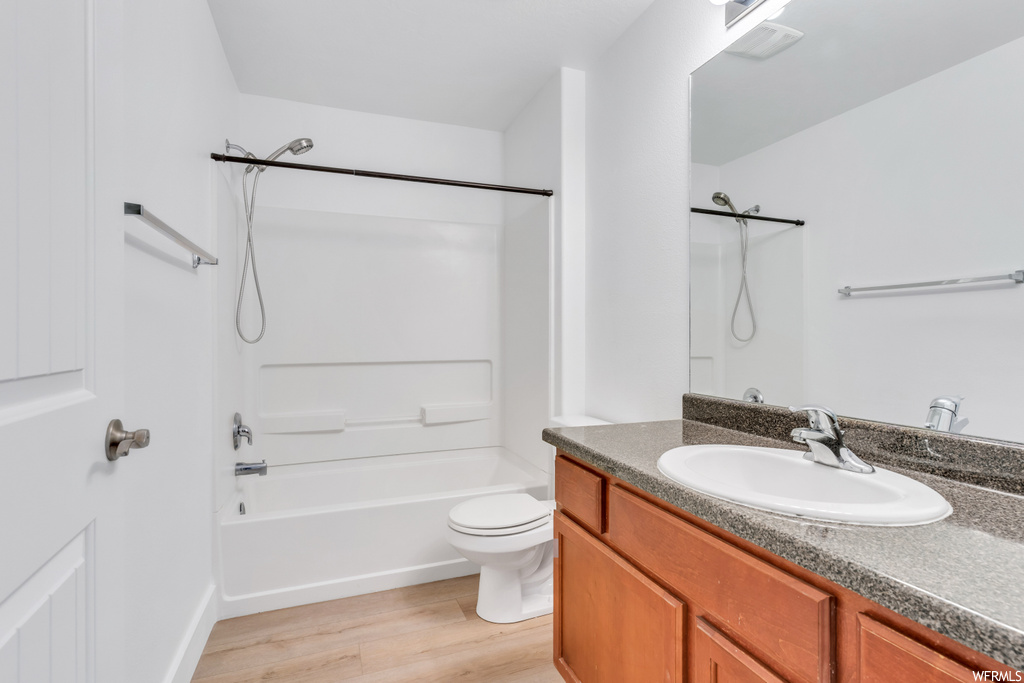 Full bathroom with wood-type flooring, toilet, vanity, and washtub / shower combination