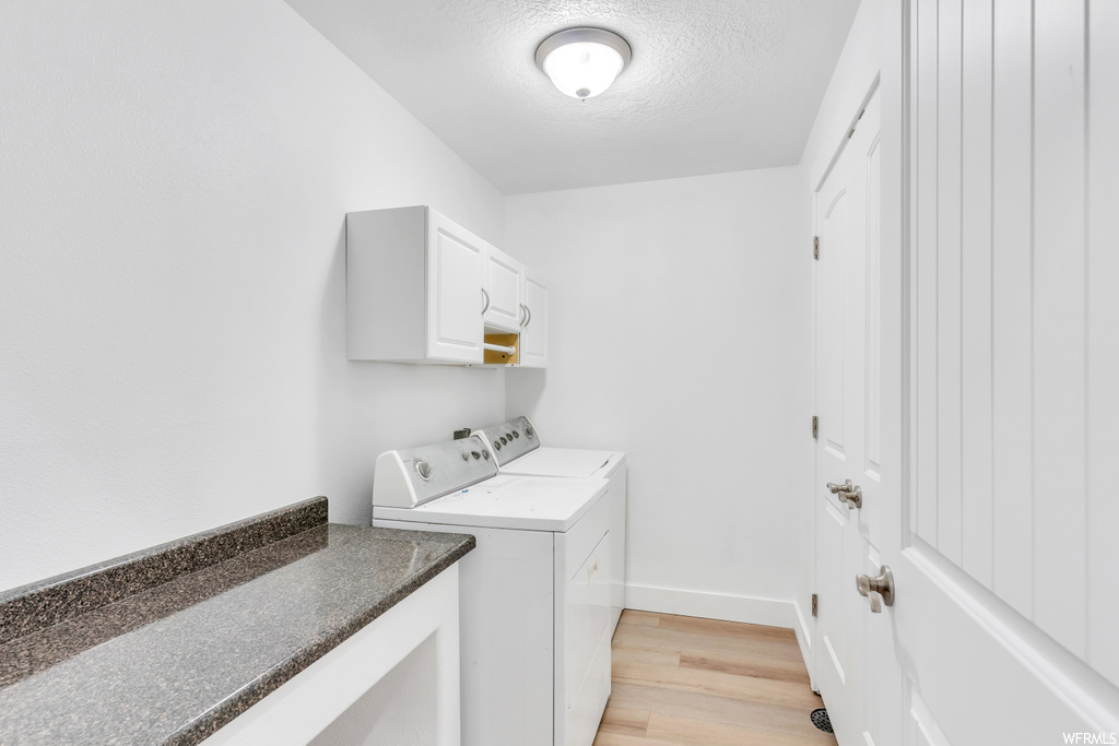 Clothes washing area with separate washer and dryer, a textured ceiling, cabinets, and light hardwood floors