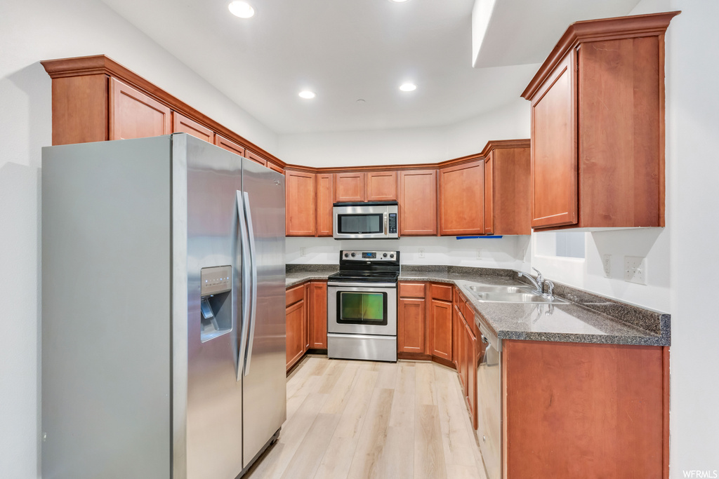 Kitchen with sink, dark stone countertops, stainless steel appliances, and light hardwood flooring