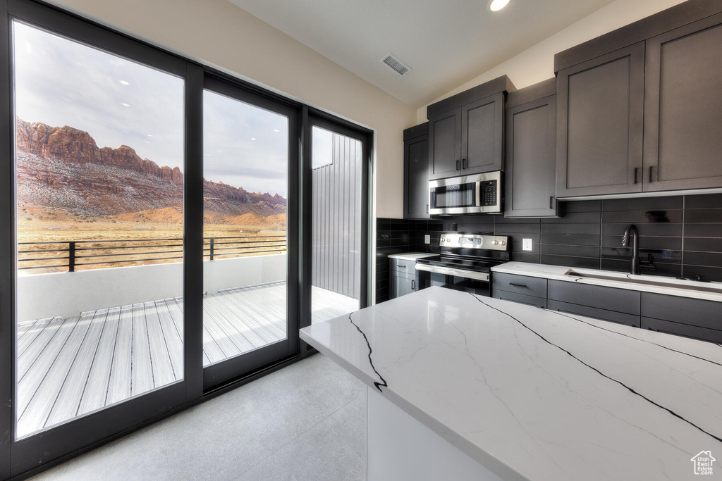 Kitchen with light stone counters, a mountain view, backsplash, appliances with stainless steel finishes, and sink