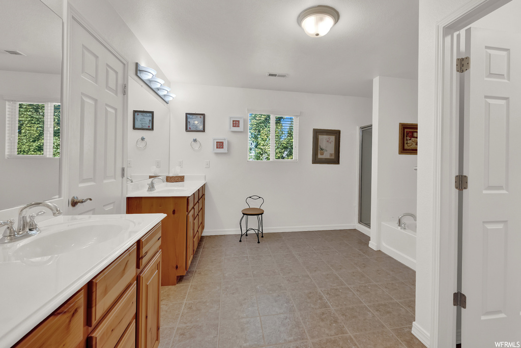 Bathroom featuring tile flooring, double sink vanity, separate shower and tub, and a wealth of natural light
