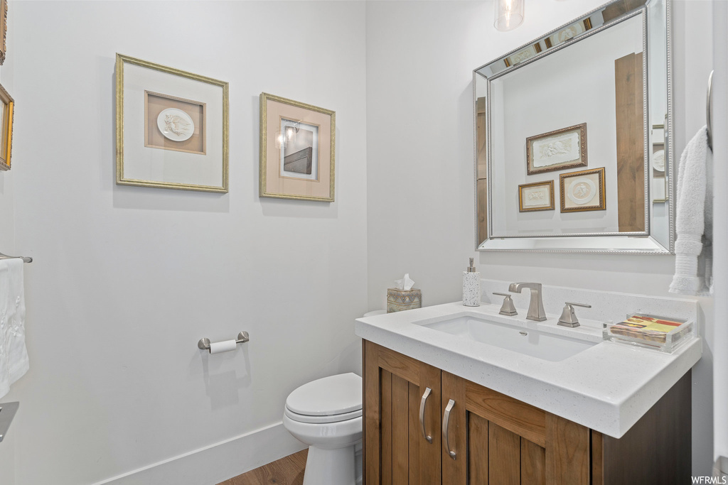Bathroom featuring toilet, vanity with extensive cabinet space, and hardwood floors
