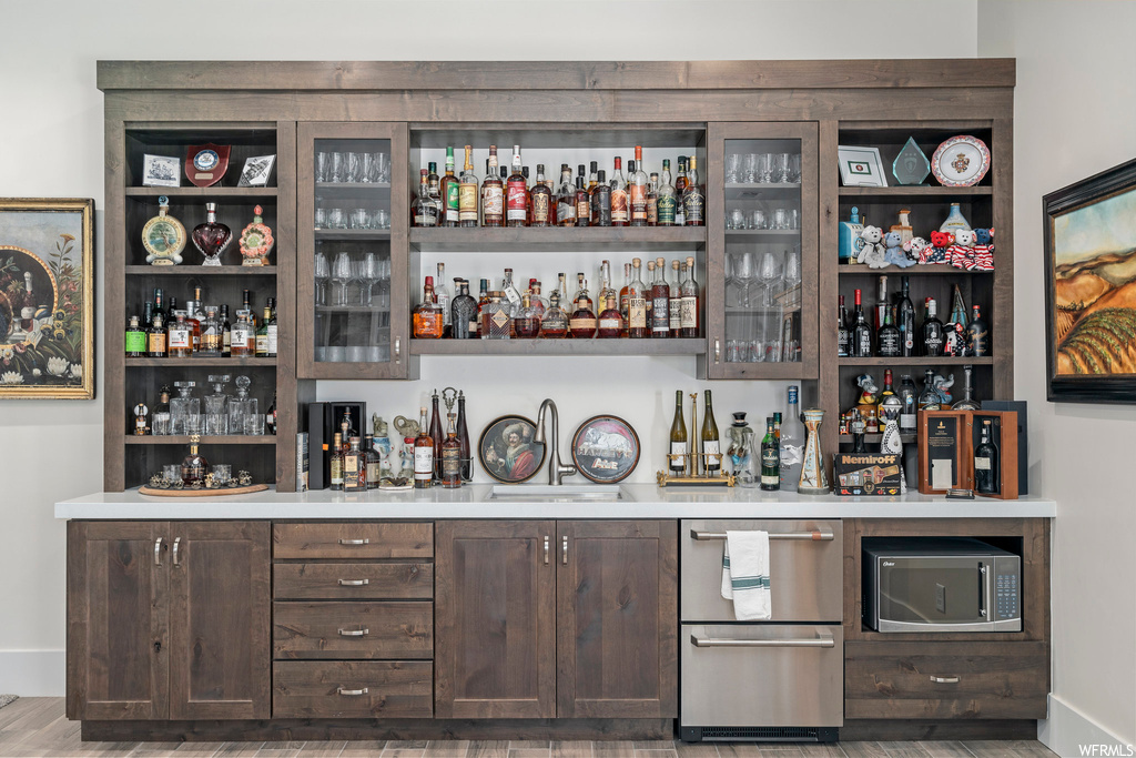 Bar with stainless steel microwave, light hardwood flooring, and dark brown cabinets