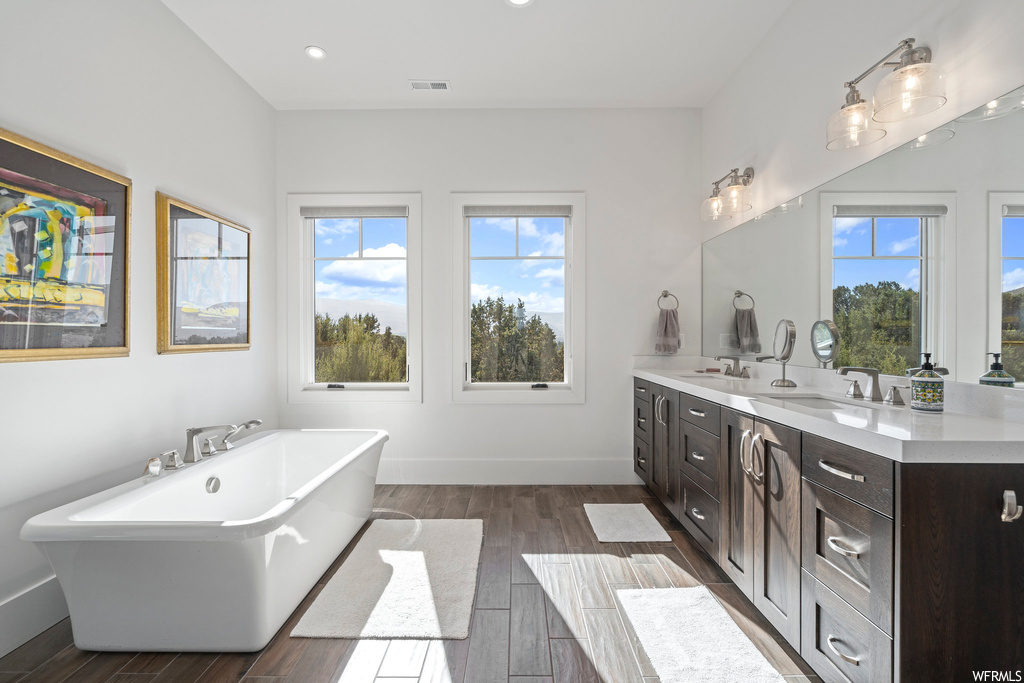 Bathroom featuring plenty of natural light, hardwood flooring, a bathing tub, and dual bowl vanity