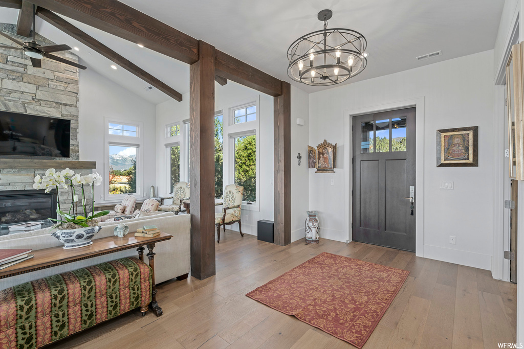 Foyer with ceiling fan with notable chandelier, hardwood floors, a wealth of natural light, and a fireplace