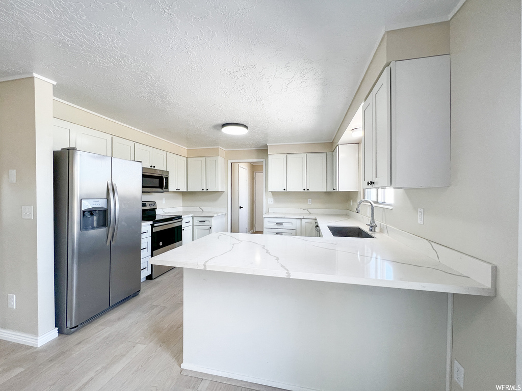 Kitchen featuring sink, light hardwood floors, white cabinetry, stainless steel appliances, and kitchen peninsula