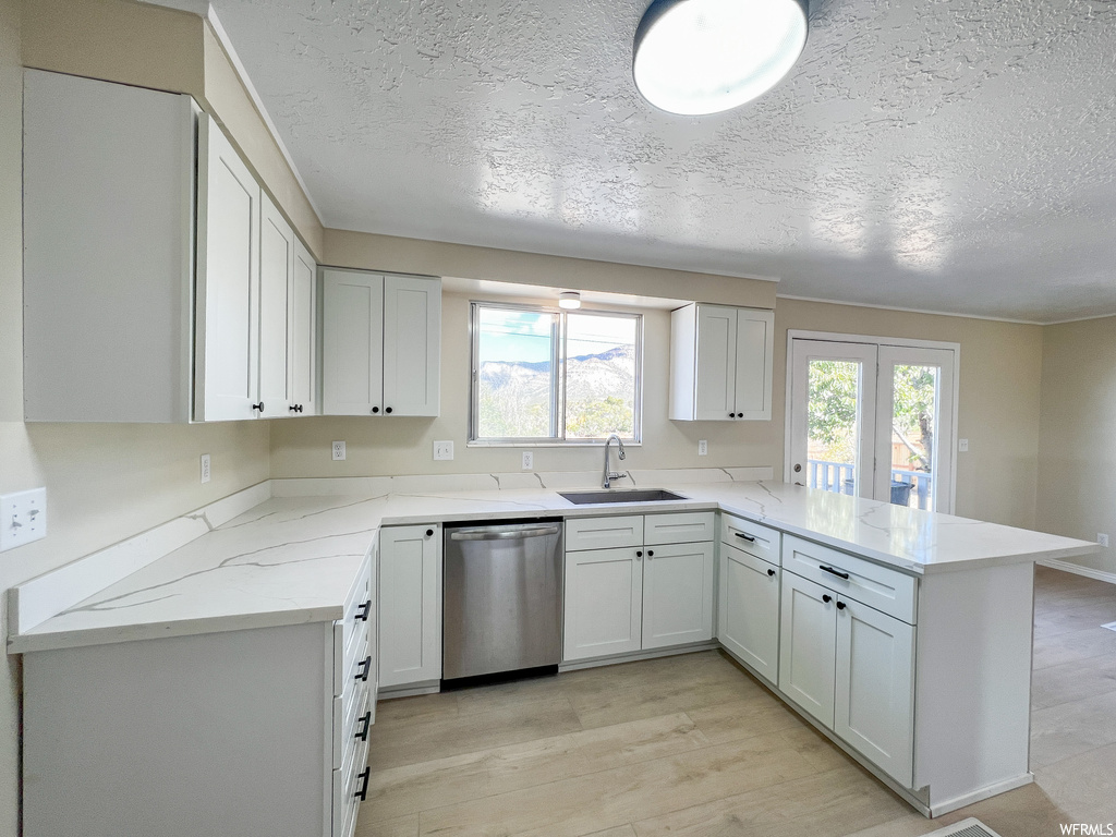 Kitchen featuring sink, light hardwood flooring, white cabinetry, stainless steel dishwasher, and kitchen peninsula