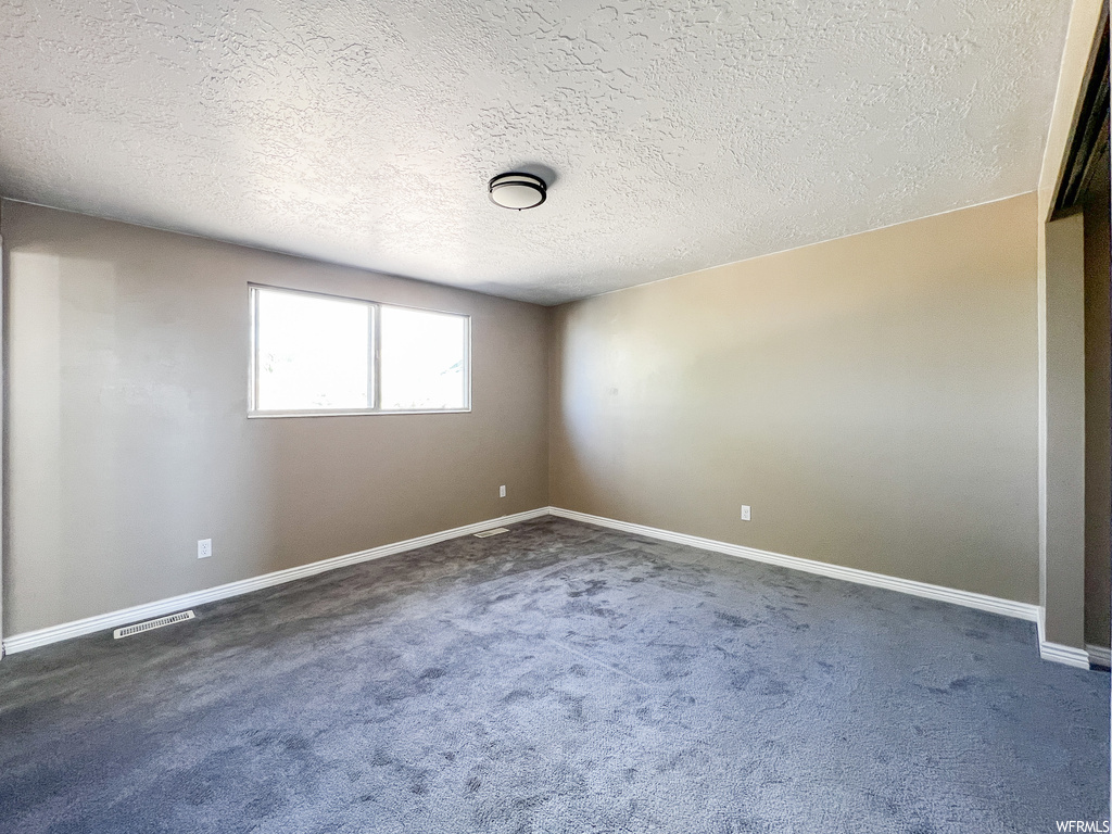 Spare room featuring dark carpet and a textured ceiling