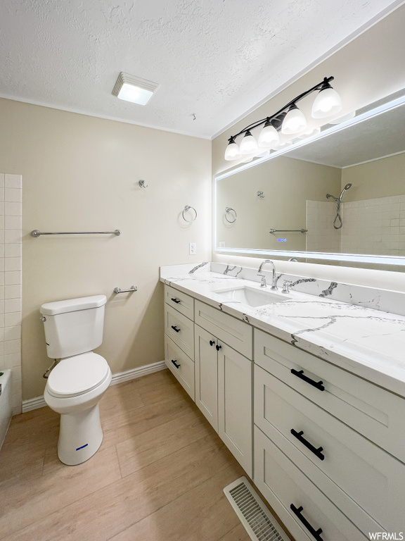 Full bathroom featuring toilet, a textured ceiling, tiled shower / bath, oversized vanity, and hardwood floors