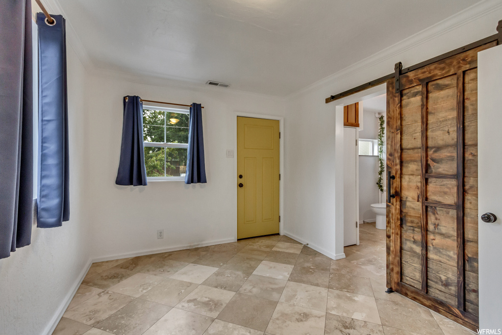 Tiled empty room featuring a barn door and ornamental molding
