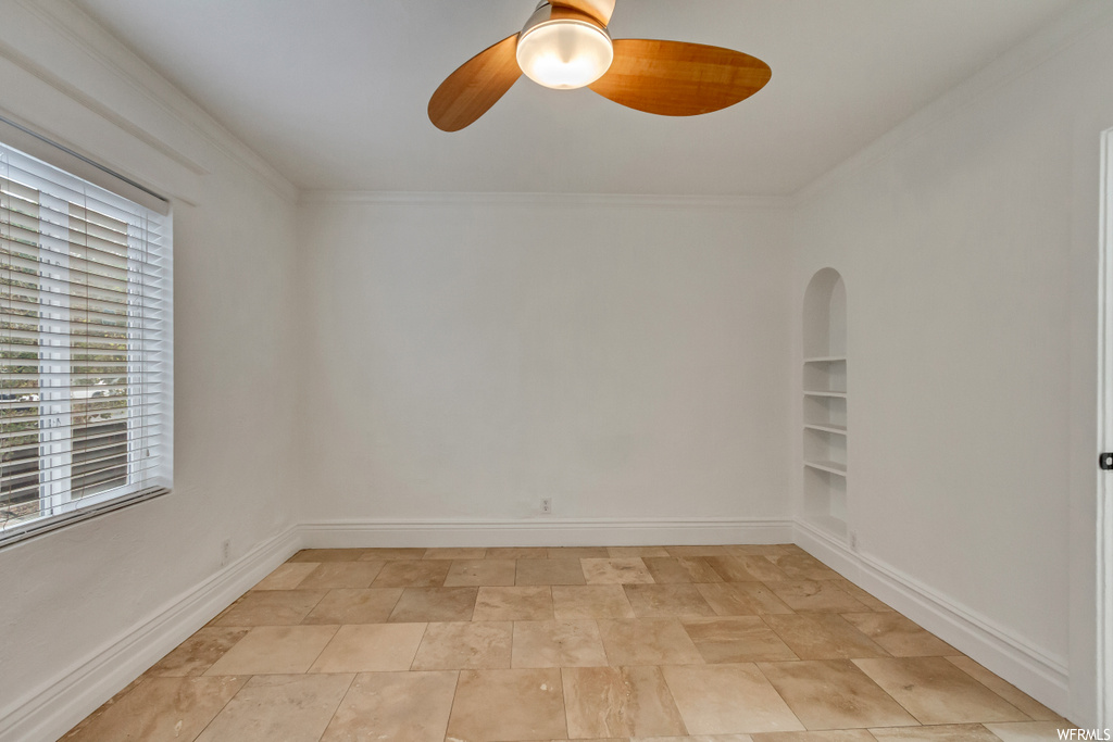 Empty room featuring built in features, ceiling fan, and light tile floors