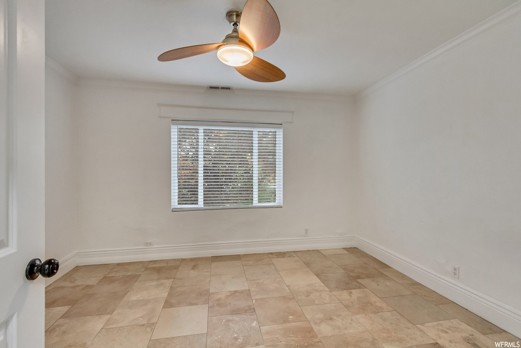 Tiled empty room with ceiling fan and ornamental molding