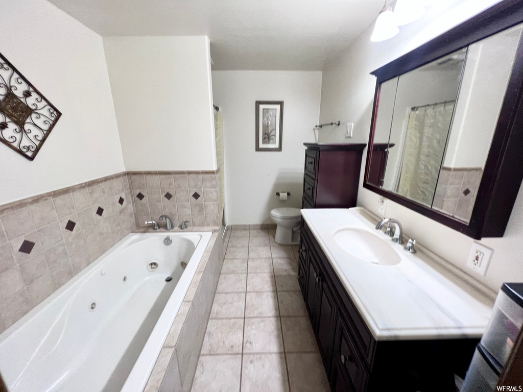 Bathroom with tiled bath, vanity, tile flooring, and toilet