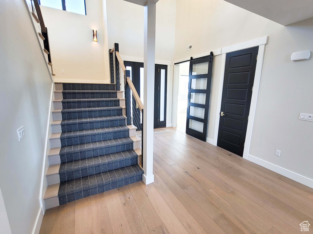 Stairs featuring a barn door, light hardwood / wood-style floors, and a towering ceiling