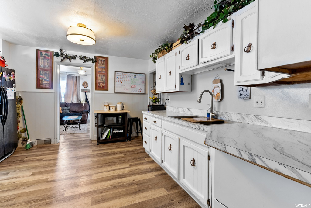 Kitchen featuring sink, white cabinets, light hardwood floors, and black appliances