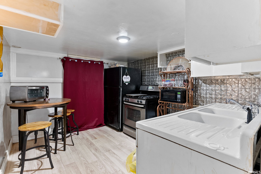 Kitchen with sink, tasteful backsplash, black appliances, and light hardwood flooring