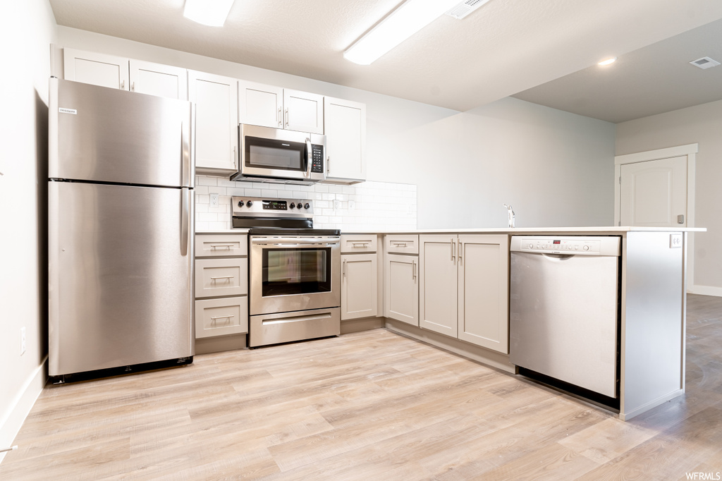 Kitchen with white cabinets, light hardwood flooring, tasteful backsplash, stainless steel appliances, and kitchen peninsula